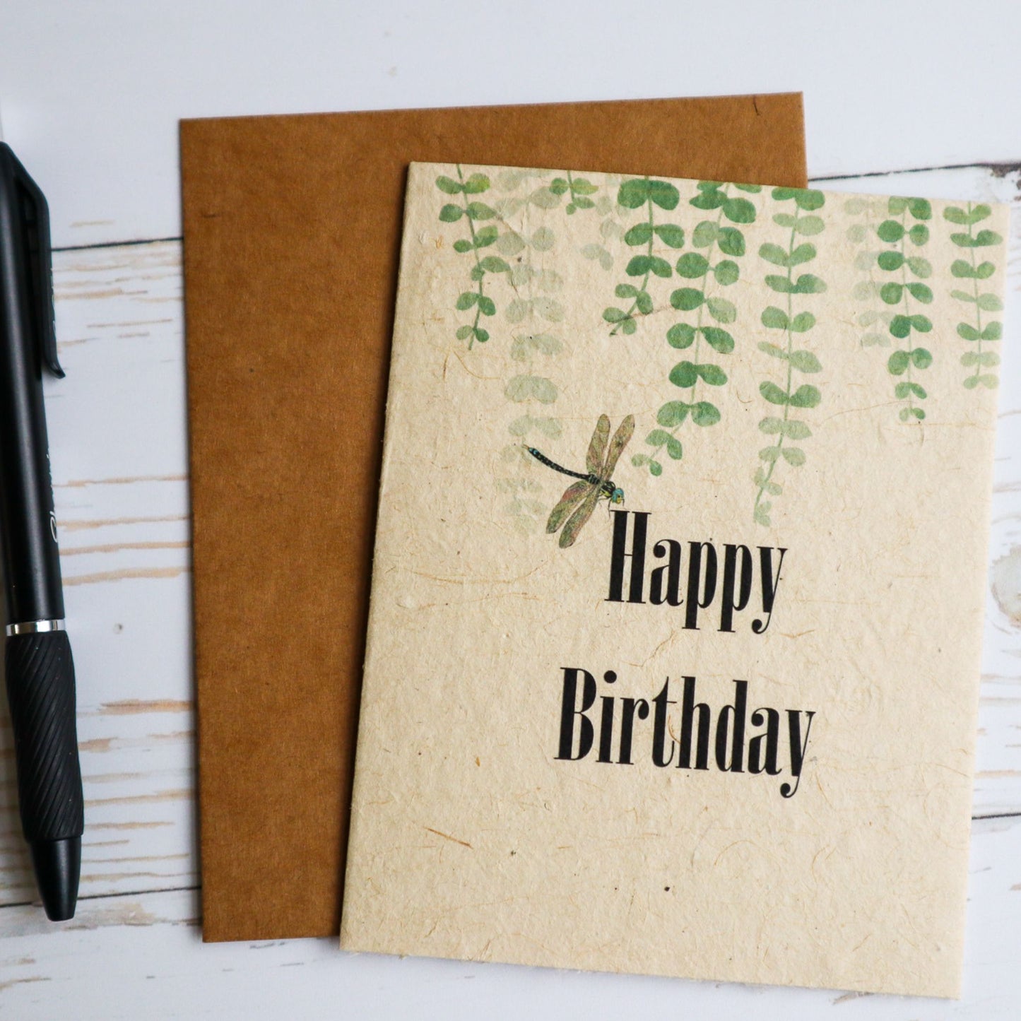 Plantable seed paper birthday card with dragonfly and greenery. Writing pen beside card.